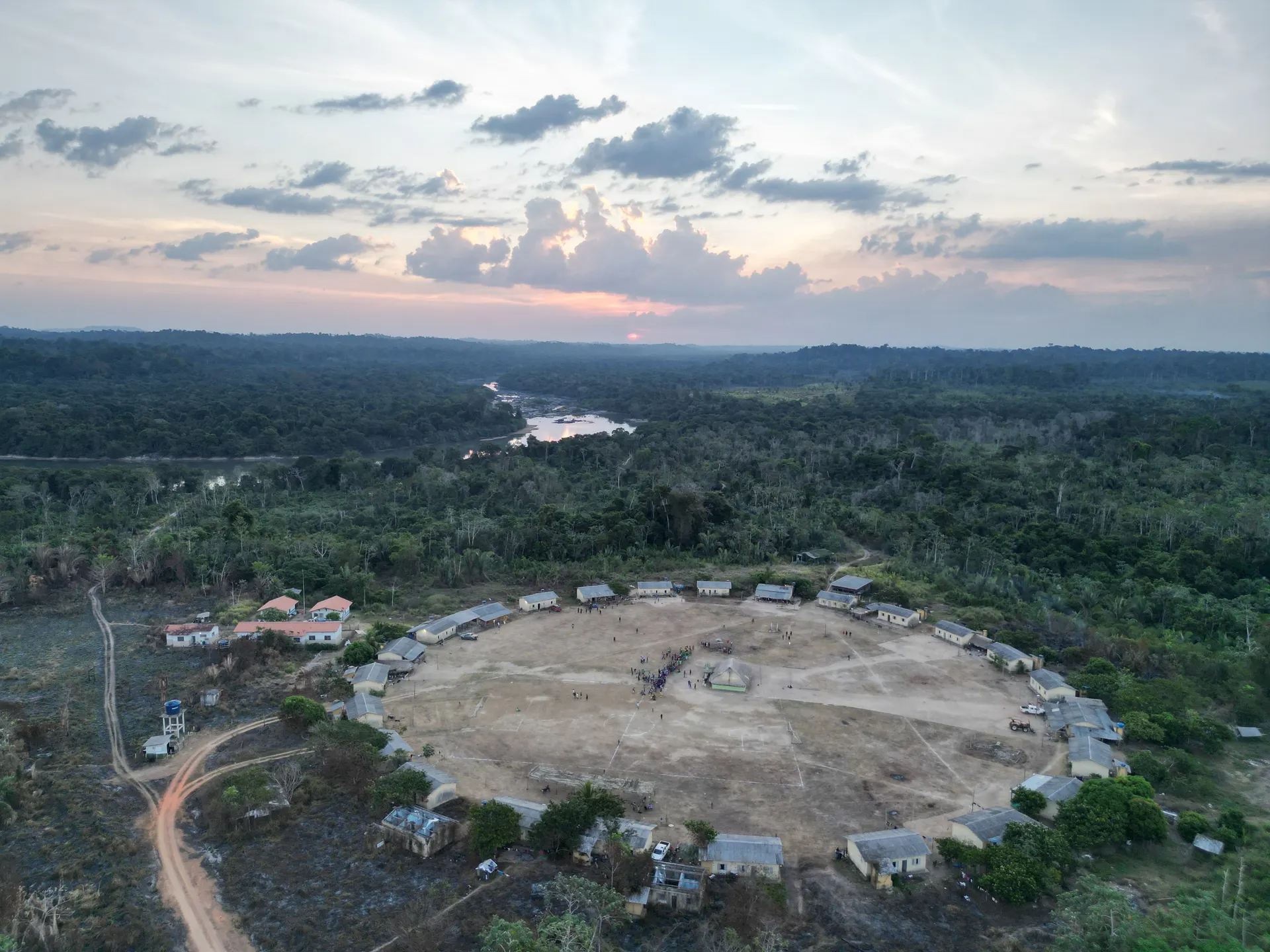 Aerial view of a circular Xikrin village at sunset, surrounded by forest, with the Bacajá River in the background
