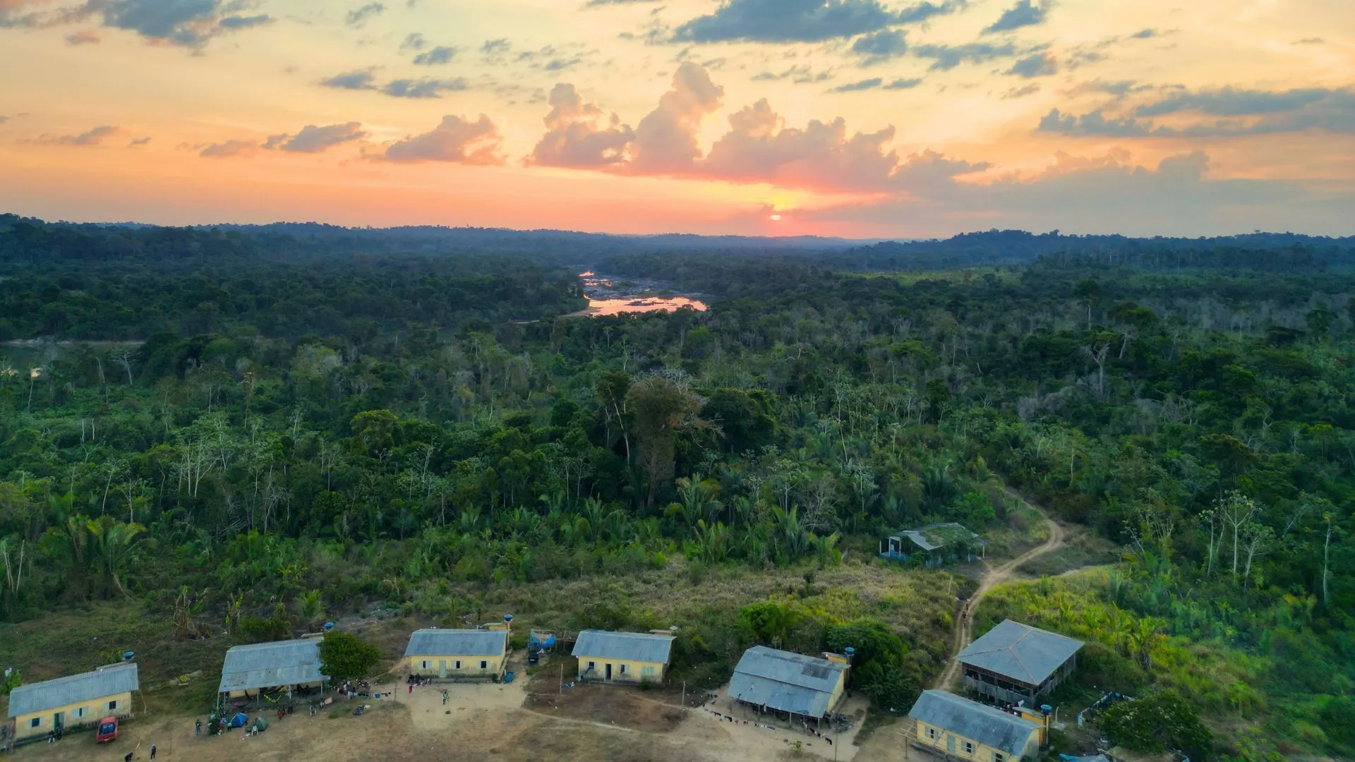 Casas da aldeia diante da floresta e do rio ao pôr do sol