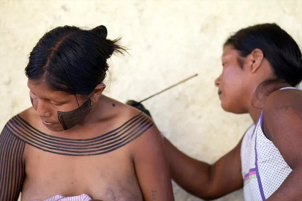 Mulher Xikrin pinta o corpo de uma jovem com jenipapo